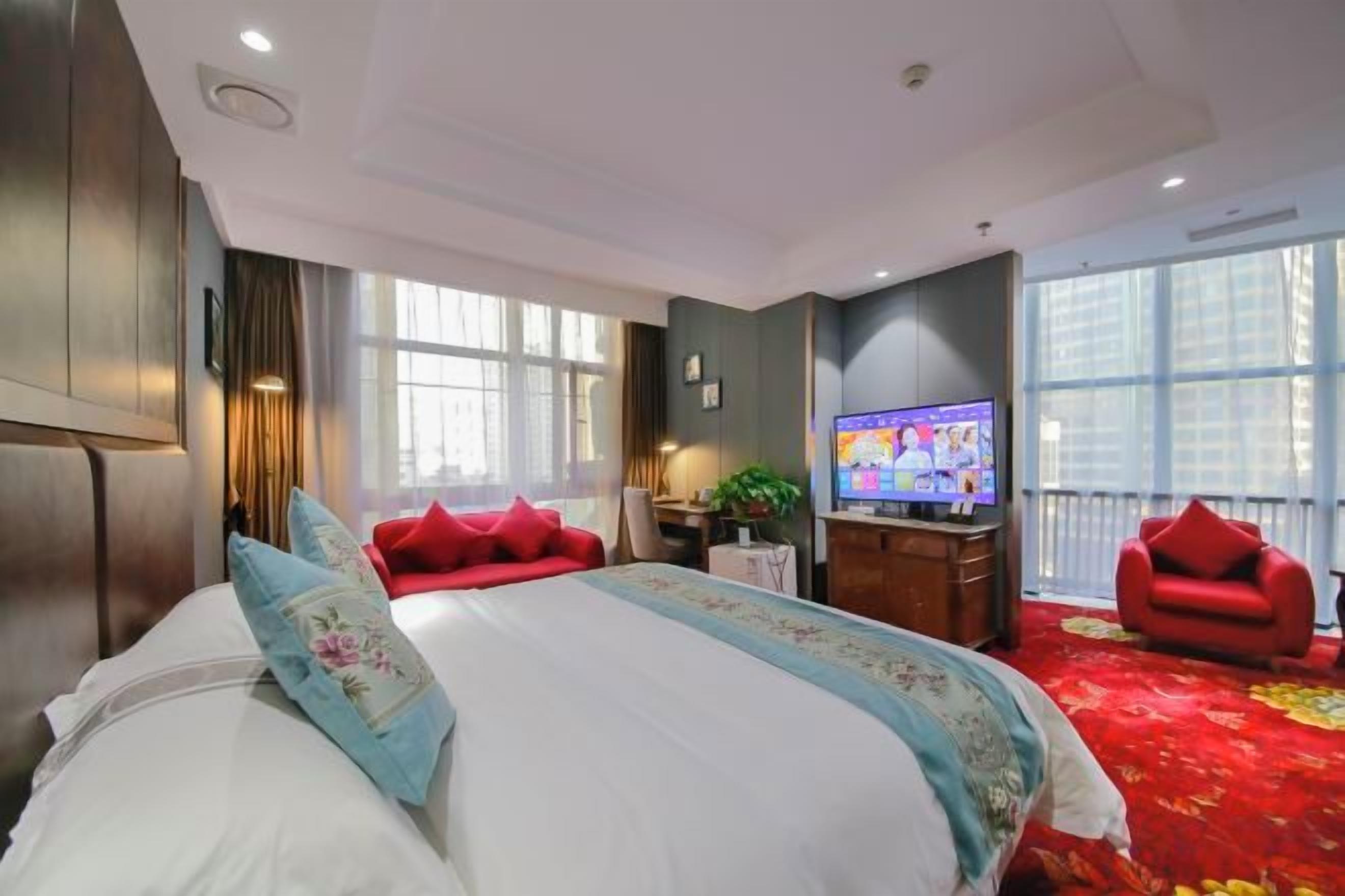 Habitación de hotel con una cama grande, televisión, sofá rojo y balcón.