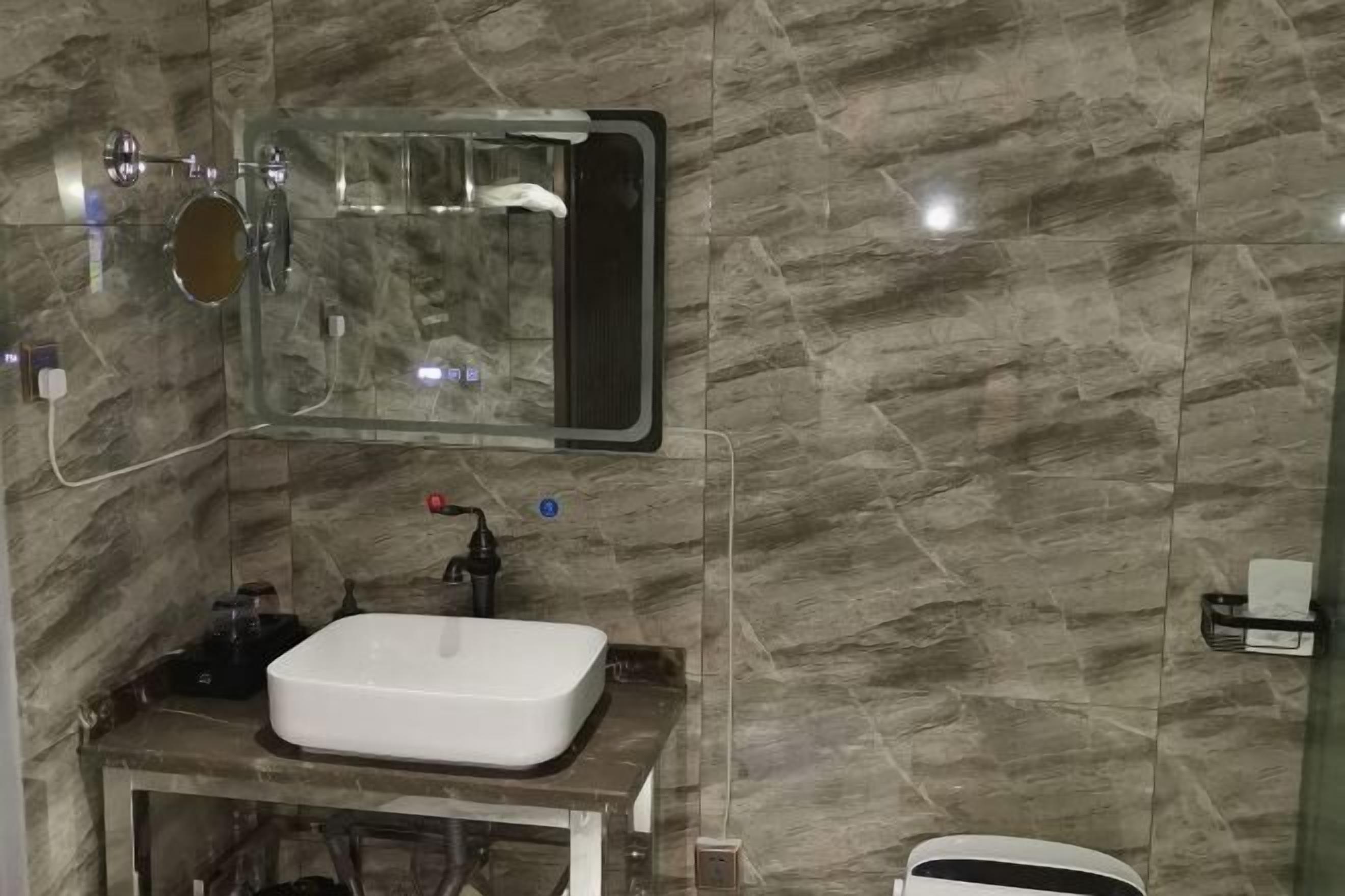 A bathroom with a marble wall, a white sink, a mirror, and a handheld showerhead.