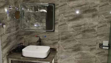 A bathroom with a marble wall, a white sink, a mirror, and a handheld showerhead.