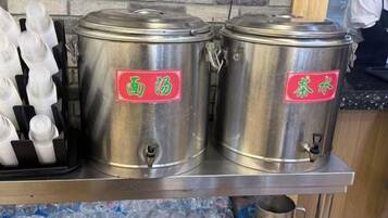Recipientes de aço inoxidável com etiquetas, uma bandeja de copos descartáveis brancos e uma bancada.