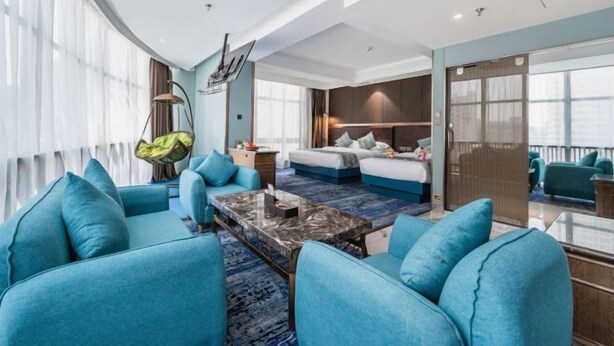 Een moderne hotelkamer met een groot bed, een zithoek met blauwe banken, een salontafel en een balkon met uitzicht.