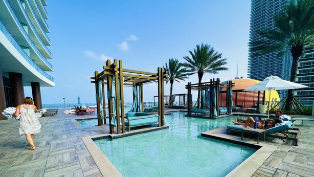 A pool area with a wooden pergola, lounge chairs, and a view of the ocean. -  Lyfe Resort & Residences (Hollywood)