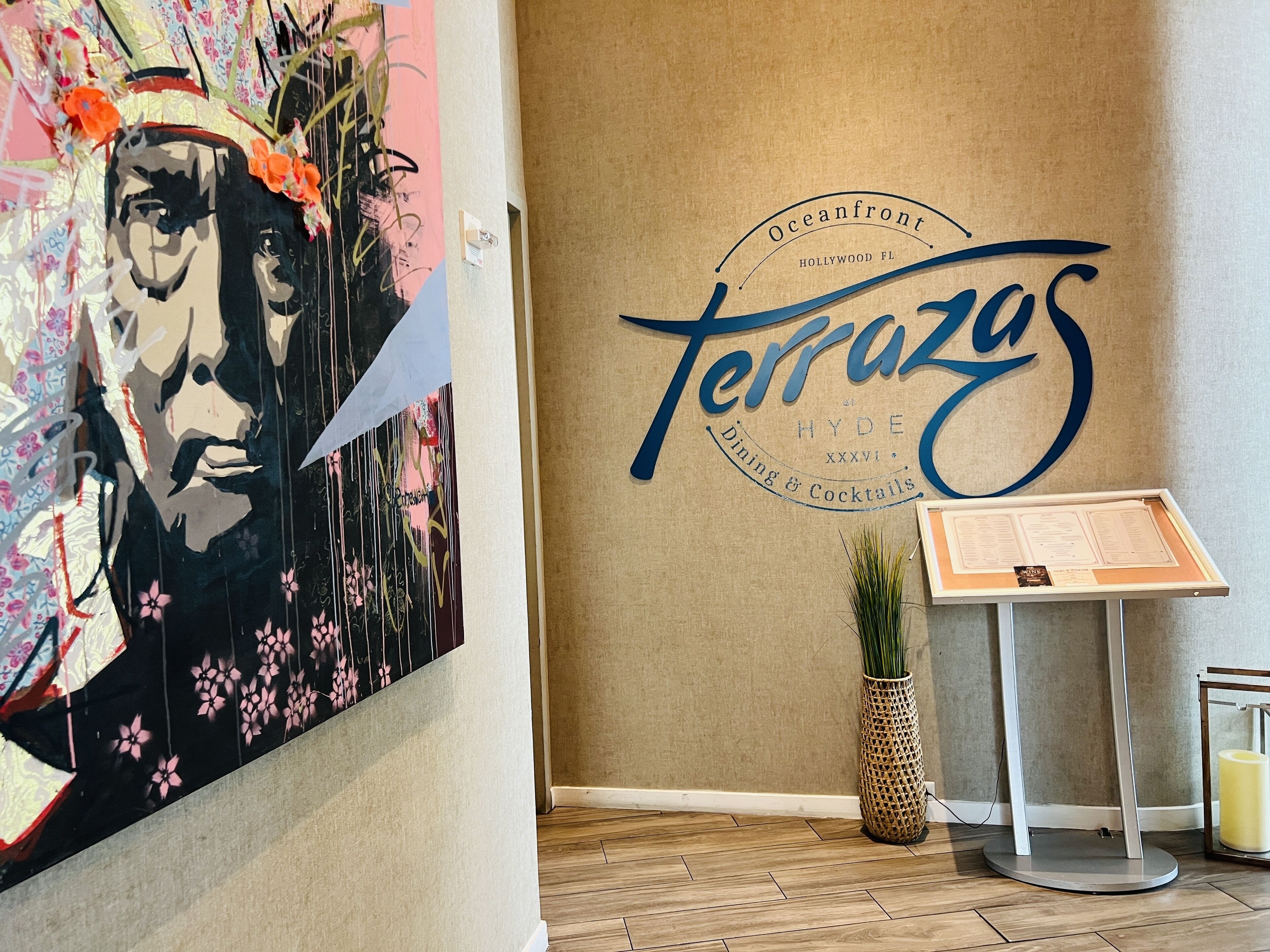 Un muro con un grande cartello 'Terrazos', una bacheca con il menu e una pianta decorativa.