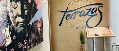 Un muro con un grande cartello 'Terrazos', una bacheca con il menu e una pianta decorativa.