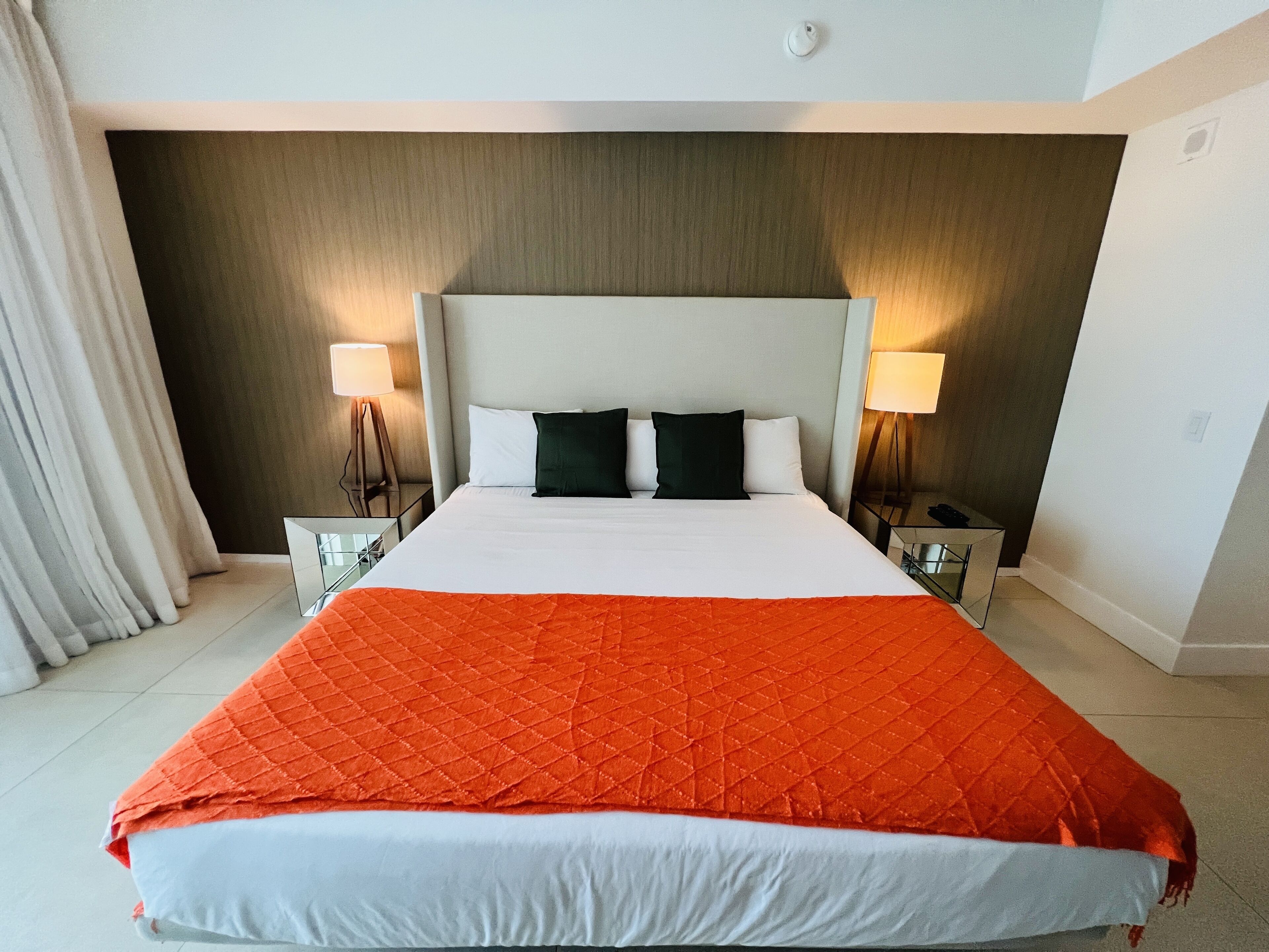 A hotel room with a large bed, two bedside tables, a nightstand, and a headboard.
