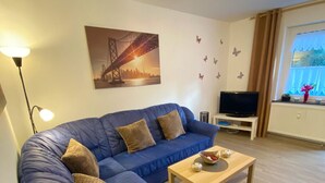 Una sala de estar moderna con un sofá azul, una mesa de centro de madera, una televisión y un cuadro de un puente en la pared.
