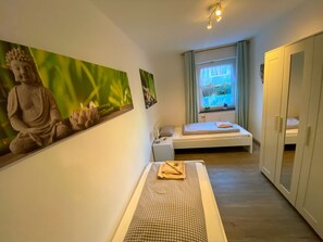 Una habitación pequeña y limpia con una cama, un banco de meditación, una estatua y una ventana con vistas.