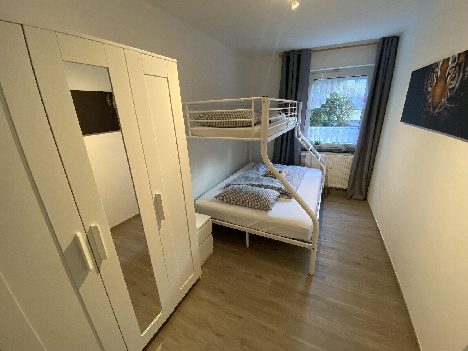 A bedroom with a bunk bed, a wardrobe, a radiator, and a window with curtains.