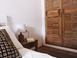 A bedroom with a bed, a bedside table with a lamp, a book, and a wooden wardrobe. - Amazing villa near the beach (Binibequer)