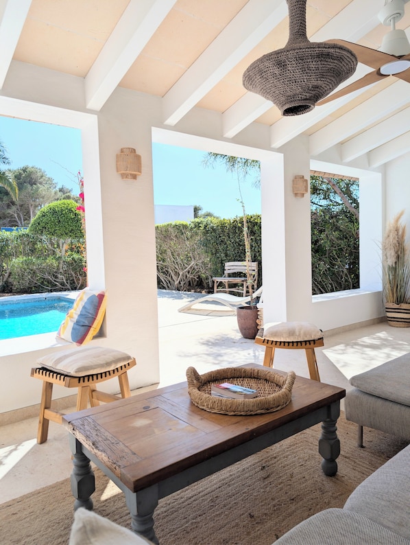 Une terrasse ensoleillée avec vue sur la piscine, dotée de mobilier en bois et de paniers tressés.