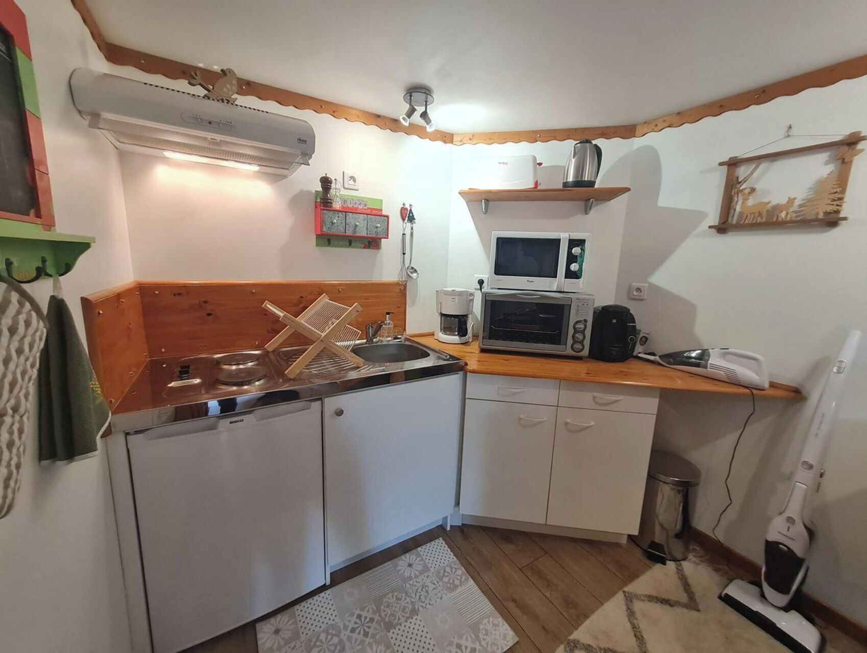 A compact kitchen with white cabinets, a wooden countertop, a microwave, a coffee maker, and a sink.