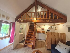 A cozy interior with a wooden staircase leading to a loft bedroom, a kitchen area, and a living space with a sofa and a pillow with "HOPE" on it.