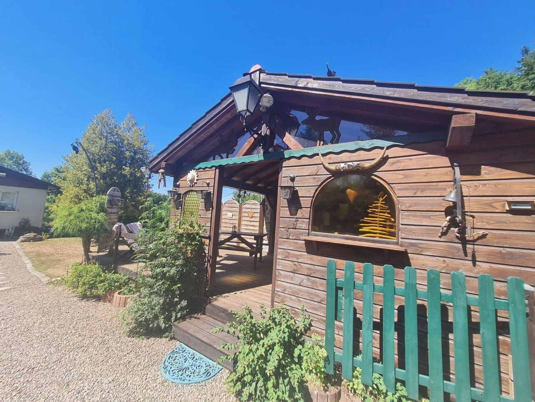 A rustic wooden building with a porch, a small window with a decorative item inside, and a green picket fence.