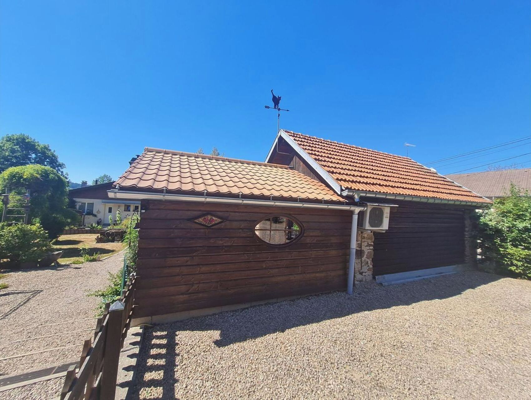 Une cabane en bois avec un toit recouvert de tuiles, une fenêtre ronde et une girouette.