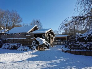 A wooden cabin with a snow-covered roof and a wooden fence in a snowy landscape.