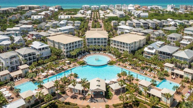 An aerial view of a resort with multiple buildings, a central swimming pool, and surrounding palm trees. - Hemingway at 30A - Seacrest, 12,000 Sq Ft Community Pool, Beach Tram, Bikes! (Seacrest Beach)