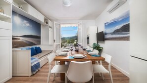 Un comedor con vistas al mar, muebles blancos y una mesa de madera dispuesta para una comida.