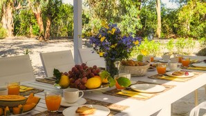 Una mesa de desayuno al aire libre con frutas, flores y bebidas.