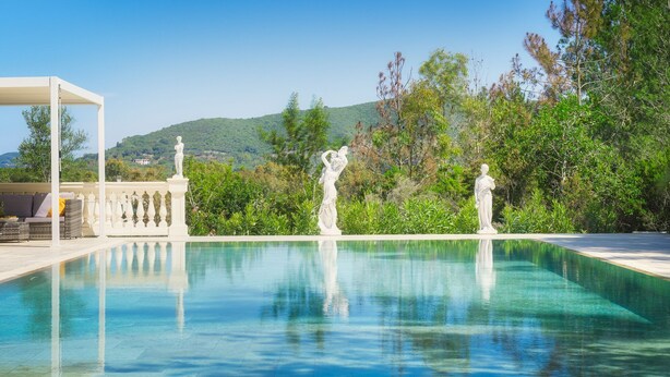 Una piscina con estatuas, una zona de estar techada y vistas a colinas verdes.