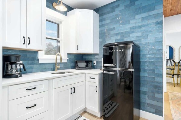 A modern kitchen with white cabinets, a black refrigerator, a microwave, and a coffee maker.