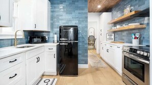 A modern kitchen with white cabinets, a black refrigerator, and a wooden ceiling.