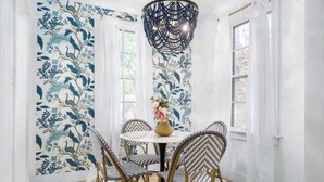 A dining area with a round table, four chairs, a decorative vase, and a patterned wallpaper.