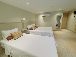 Une chambre d’hôtel avec deux lits simples, une table de chevet, une lampe, un appareil de climatisation et un miroir.