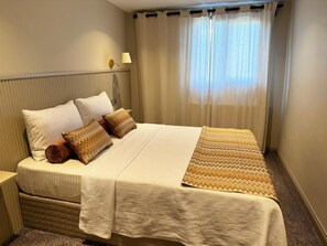 Ein Hotelzimmer mit Bett, Nachttisch, Lampe und einem Fenster mit Vorhängen.