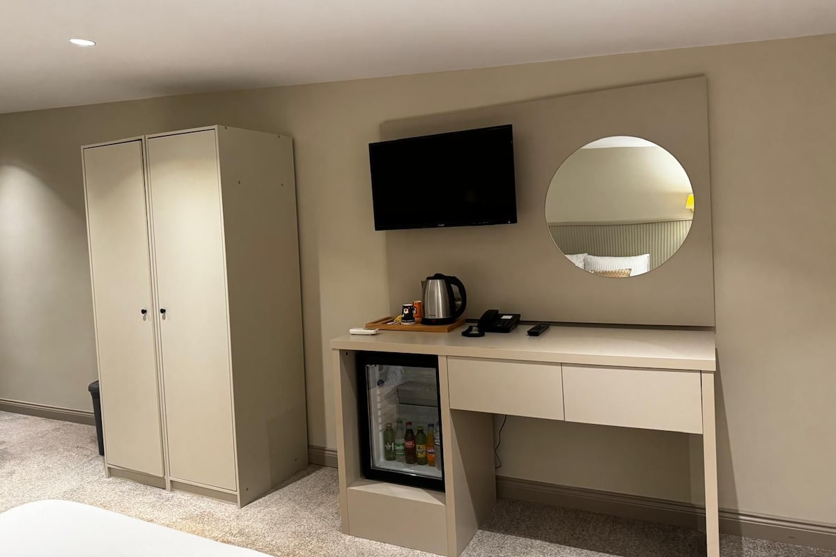 Ein Hotelzimmer mit Schrank, Schreibtisch mit Spiegel, Fernseher und Minibar.