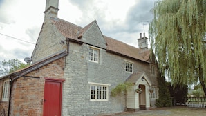 A stone house with a red door, a small porch, and a weeping willow tree. - Kestrel Cottage in Castle Ashby (Northampton)