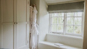 A bathroom with white cabinets, a window with a view of greenery, and a white bath mat on the floor. - Kestrel Cottage in Castle Ashby (Northampton)