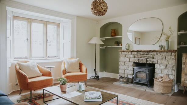 A living room with a fireplace, two armchairs, a coffee table, and a large window. - Kestrel Cottage in Castle Ashby (Northampton)