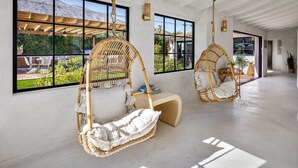 A spacious room with large windows, two wicker hanging chairs, and a wooden bench. - Casa De Tierra - Featured in Architectural Digest (Palm Springs)
