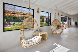 A spacious room with large windows, two wicker hanging chairs, and a wooden bench.
