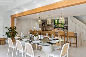 Un comedor moderno con una mesa de vidrio, sillas blancas y vigas de madera.