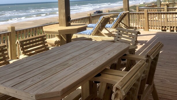 Una terraza de madera con mesas y sillas con vistas a la playa.