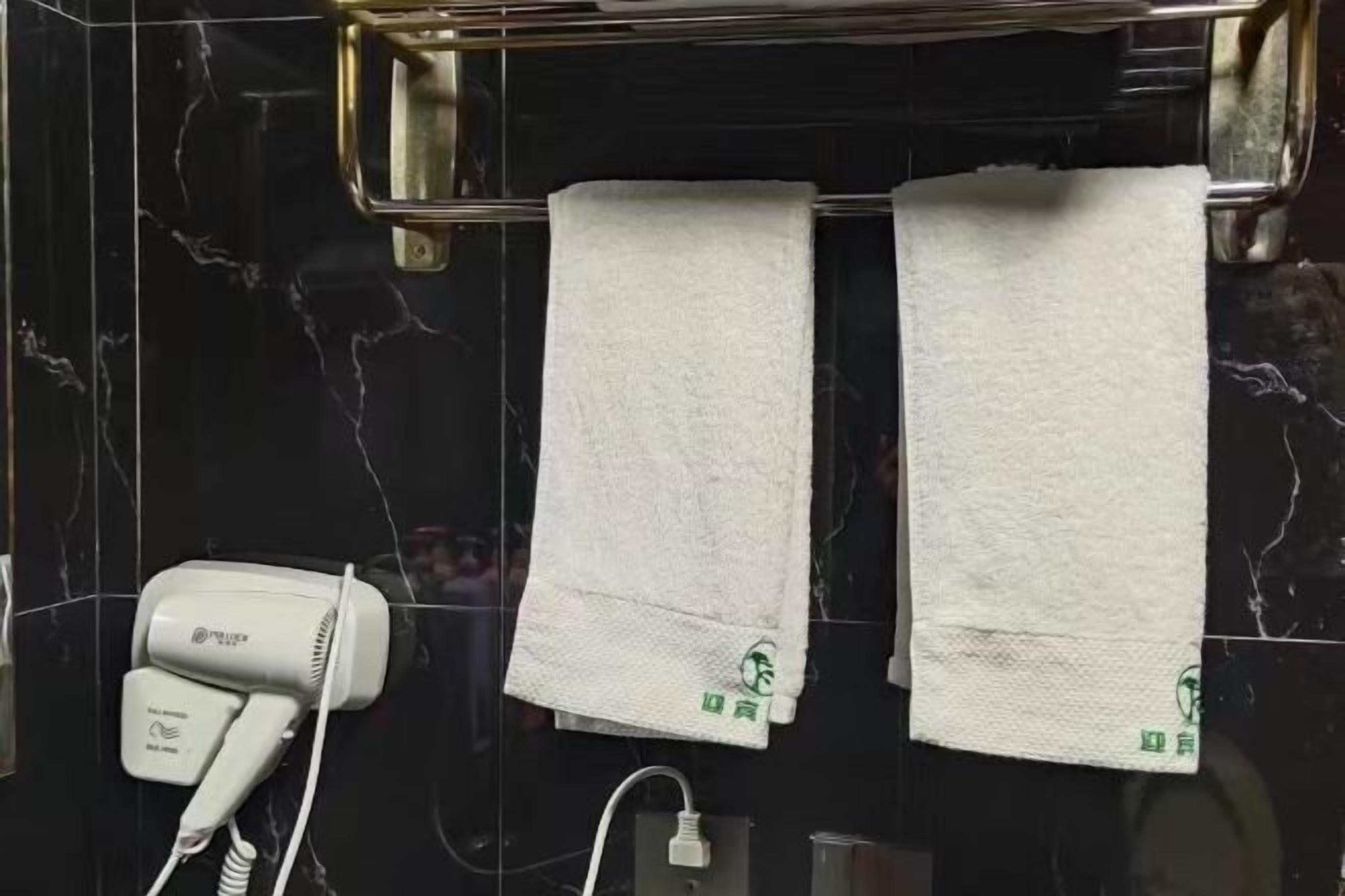 A bathroom with a hairdryer, two towels hanging on a rack, and a marble wall.