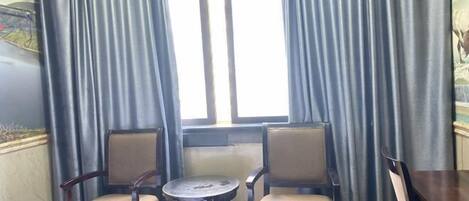 A room with two wooden chairs and a small round table, a window with curtains, and a wall-mounted air conditioner.