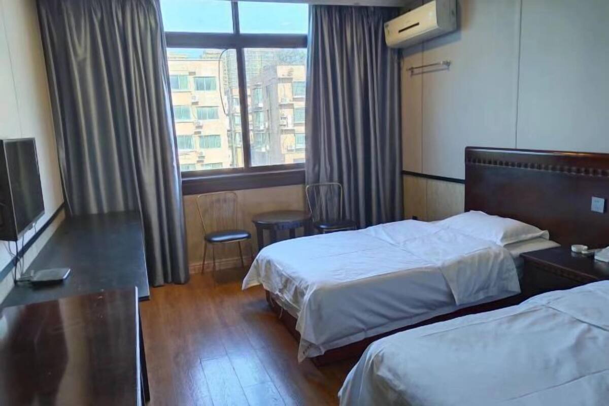 A hotel room with two beds, a desk, a chair, and a window with curtains.