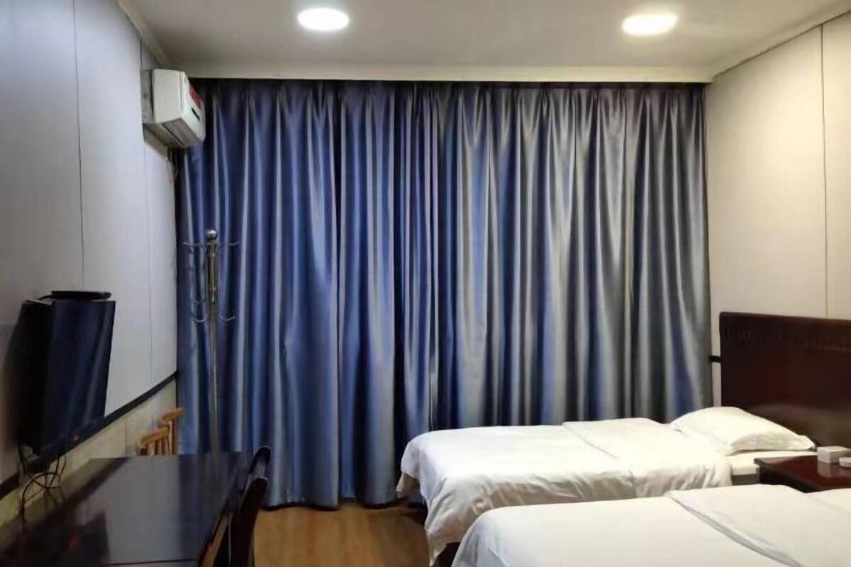 A hotel room with two beds, a flat-screen TV, a desk, and a curtain.