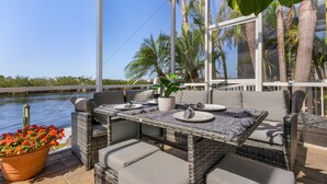 An outdoor patio with wicker furniture, a table set for two, and a view of the water and palm trees. - VILLA "EAGLE'S NEST"  THREE STORY HOME WITH AMAZING VIEWS (Cape Coral)