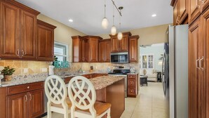 A kitchen with wooden cabinets, granite countertops, a stainless steel refrigerator, and a central island with two white chairs. - VILLA "EAGLE'S NEST"  THREE STORY HOME WITH AMAZING VIEWS (Cape Coral)