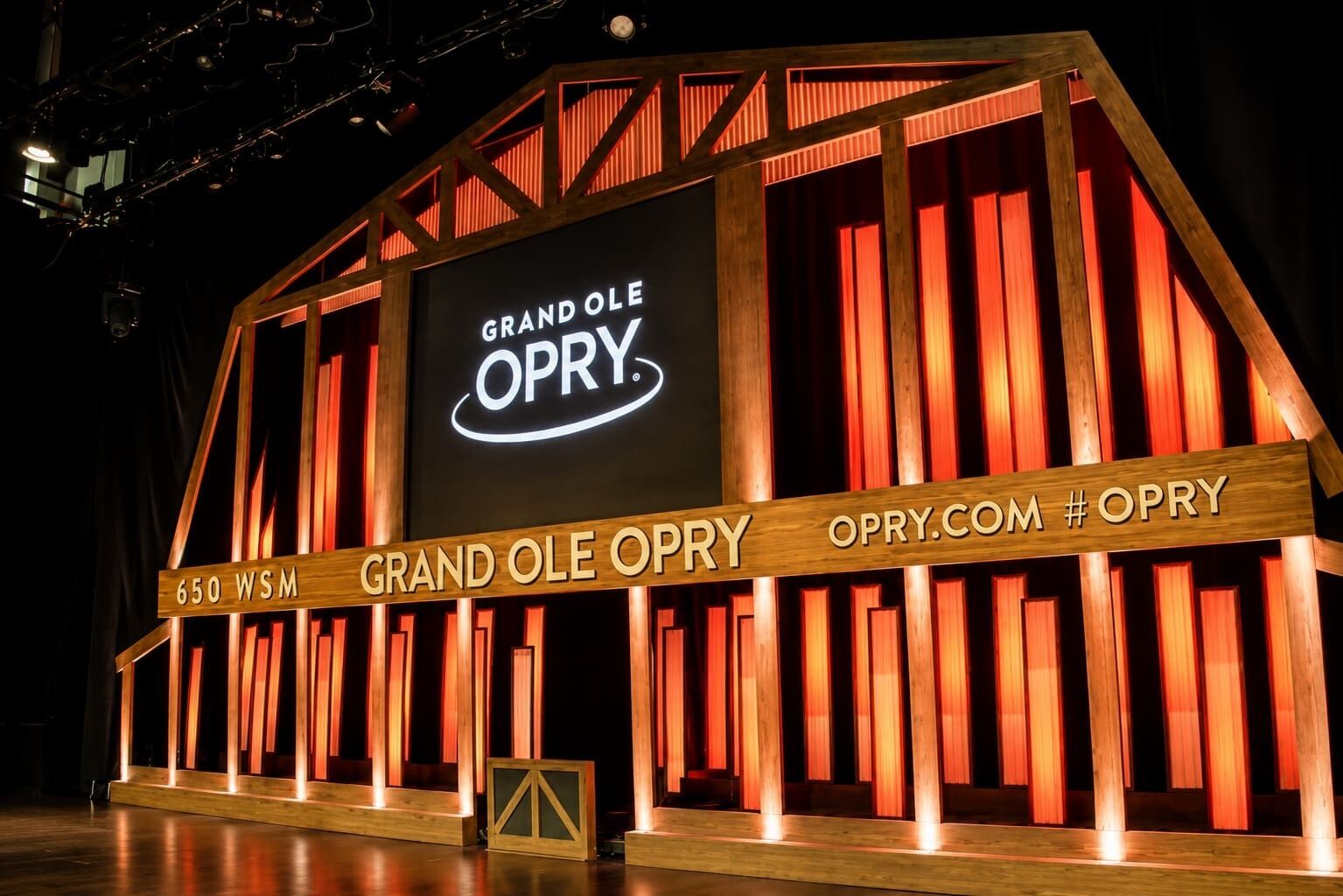 A stage with a wooden structure and a large screen displaying 'GRAND OLE OPRY' and 'OPRY.COM #OPRY'.