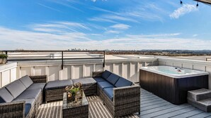 Una terraza en la azotea con mobiliario exterior, un jacuzzi y vistas al horizonte de la ciudad.