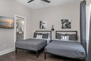 A bedroom with two beds, a ceiling fan, artwork, and a view of the outside.