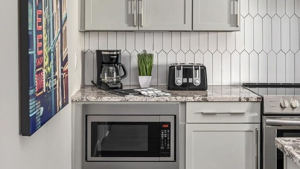 Una cocina moderna con armarios blancos, microondas, tostadora y cafetera sobre la encimera.