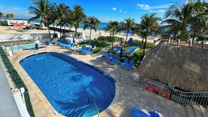 A swimming pool with lounge chairs and palm trees, surrounded by a beach and a thatched-roof structure. - Marenas Beach Resort (Sunny Isles Beach)