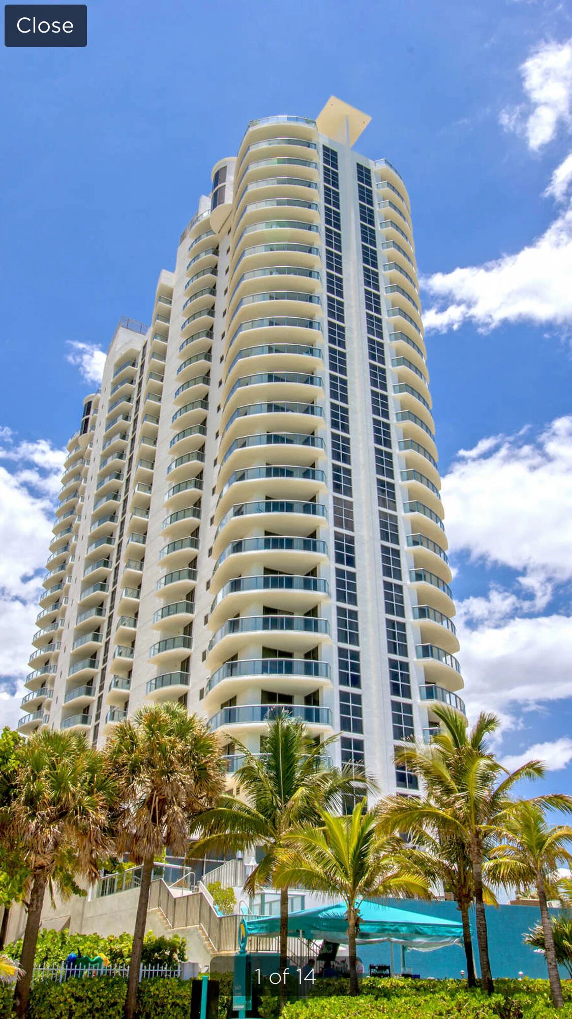 A high-rise hotel with multiple balconies, a clear sky, and palm trees in the foreground.