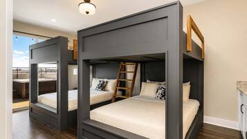 Een moderne slaapkamer met stapelbedden, een houten ladder en uitzicht op een terrasdak.