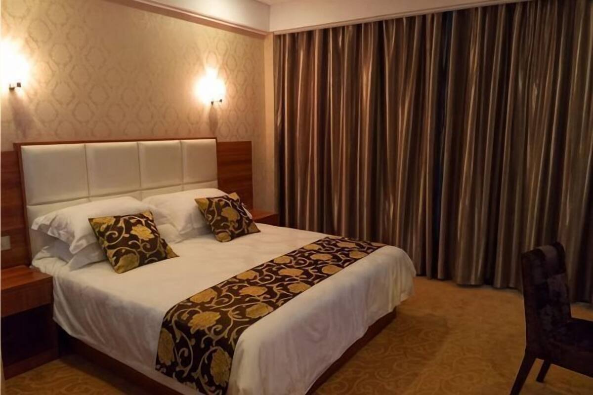 Une chambre d’hôtel avec un grand lit, deux tables de chevet, une tête de lit et un rideau.